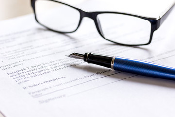 Pen and glasses lying on signed documents on office desk