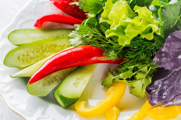 Vegetable slices with cucumber, tomatoes, paprika, lettuce, dill and herbs on white plate. Close up with selective focus