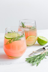 glass of fresh juice with lime and rosemary on white table background