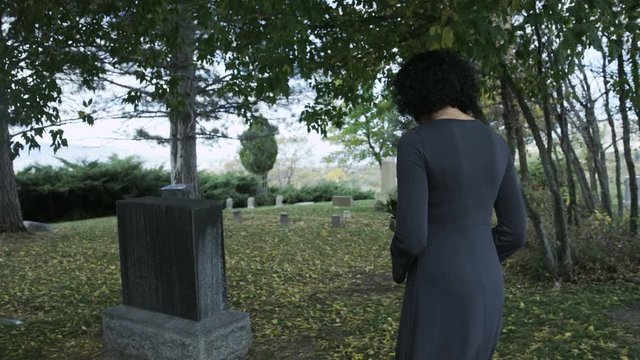 Slow motion woman placing rose on top of grave stone in Cemetary