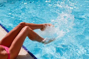 Female foot in blue water. Feet splashing in the pool. Blue water in the pool is splashes from female legs. Women's legs playing with water in a swimming pool. Woman frolicking in the pool.