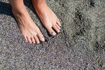 Woman feet with dark pedicure relaxing on the sand
