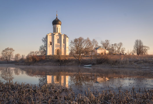 Ancient white church on the shore of the lake in the frosty dawn