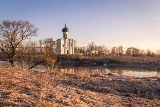 The frost on the grass blazes in the rays of the cold, blooming sun, beautifully outlining the silhouettes of trees and an ancient church