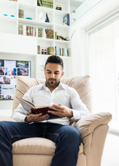 Young confident man reading book at modern home