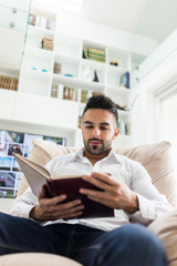 Young confident man reading book at modern home