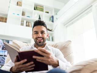 Young confident man reading book at modern home