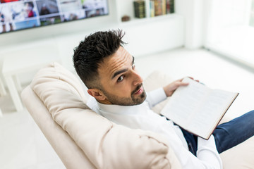 Obraz premium Young confident man reading book at modern home