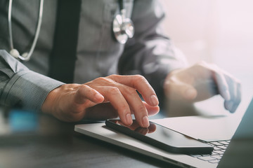 Naklejka premium bliska inteligentnego lekarza medycyny pracy z telefonem komórkowym i laptopem i stetoskopem na ciemnym drewnianym biurku