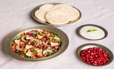 Tabbouleh salad and Arab pita bread with pomegranate seeds and white sour cream sauce against white background. Selective focus.