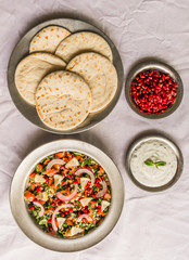 Tabbouleh salad and Arab pita bread with pomegranate seeds and white sour cream sauce against white background. Selective focus.
