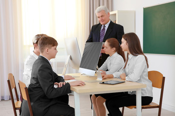 Senior teacher and pupils working with computers in classroom