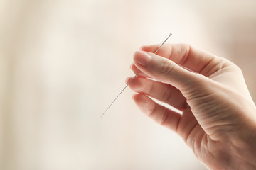 Female hand with needle for acupuncture on blurred background - obrazy, fototapety, plakaty