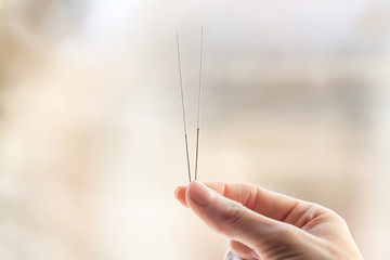 Female hand with needles for acupuncture on blurred background - obrazy, fototapety, plakaty