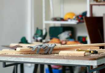Table with wooden boards and gloves in carpenter's workshop
