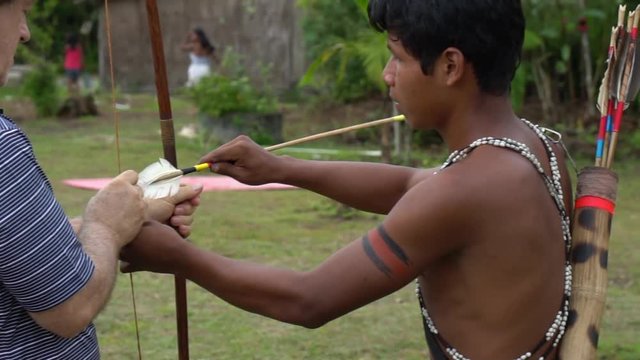 Indigenous man Teaching a Tourist how to practice Bow & Arrow in a indigenous tribe in Brazil
