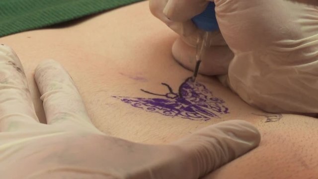 Tattoo artist drawn a butterfly on a woman's belly