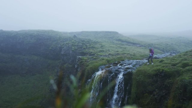 woman filtering water at edge of waterfall in Icelandic mountain stream