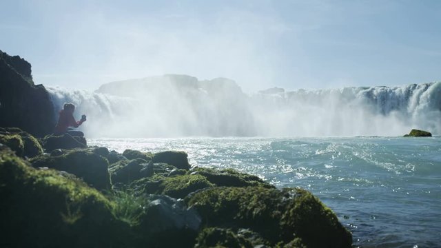Woman taking photos of Godafoss waterfall in Iceland