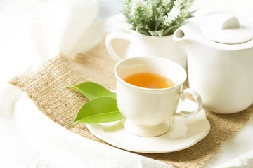 Rolgordijnen Thee Close-up van biologische thee in witte kop met groen blad, theeceremonie tijdconcept