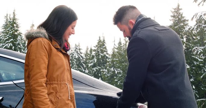 Couple talking while charging the electric car on a snowy day