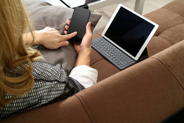 brunette woman using smart phone and digital tablet computer on sofa in living room
