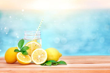  Citrus lemonade water with lemon sliced , healthy and detox water drink in summer on wooden table with blue lighten blur sea background - obrazy, fototapety, plakaty