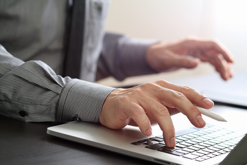 close up of businessman working with mobile phone and stylus pen and laptop computer  on wooden desk in modern office