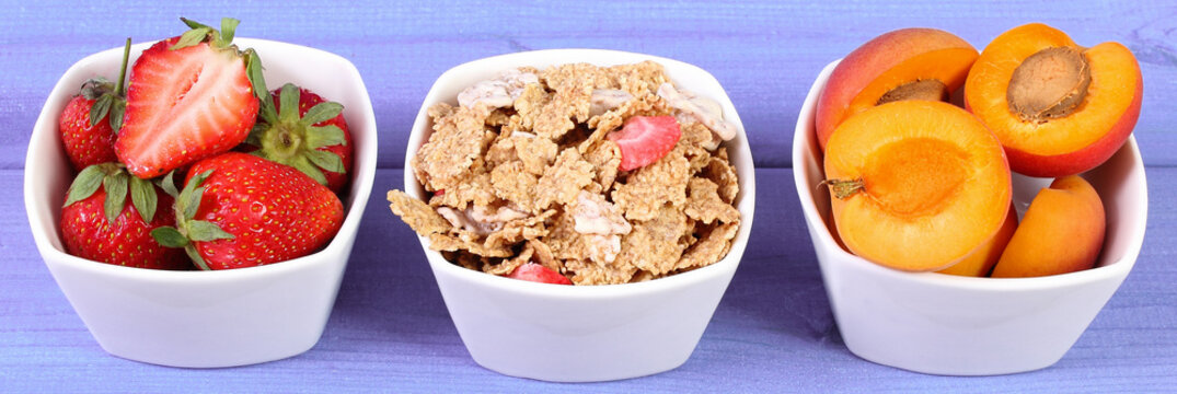 Fresh fruits, wheat and rye flakes in bowl on purple boards, healthy lifestyle
