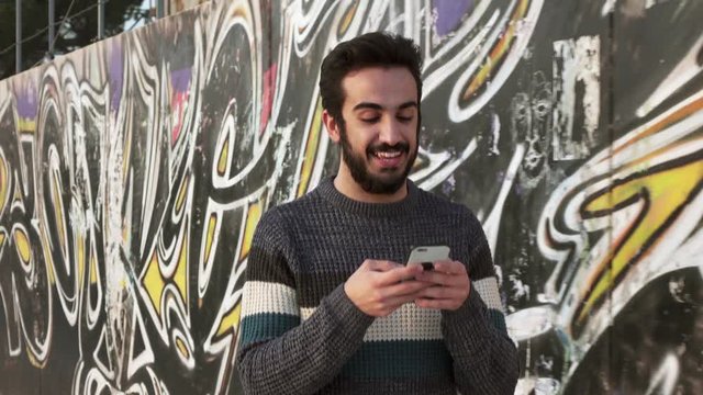 Young bearded smiling man walking on the street chatting with cellphone