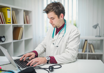 Busy young doctor working on laptop in his office alone