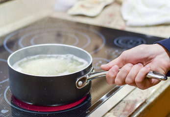 Hand picking up pot or saucepan of boiling water