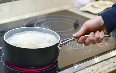 Hand picking up pot or saucepan of boiling water