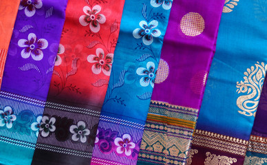 Closeup of indian latest sarees or saris hung in front of retail clothes shop or store on road in the open market 
