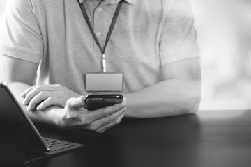 businessman in pink t-shirt working with smart phone and digitl tablet computer on wooden desk in modern office,black and white