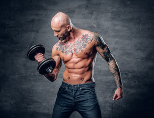 Fototapeta na wymiar Positive shaved head shirtless male dressed in a jeans holds the dumbbell.