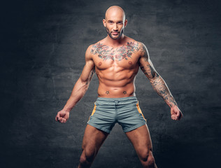 Shaved head shirtless muscular male with tattooed body.