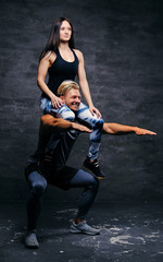 Sporty male doing squats with slim fit female on his shoulders.