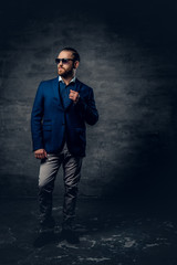 Full body studio portrait of stylish bearded male dressed in a suit and sunglasses.