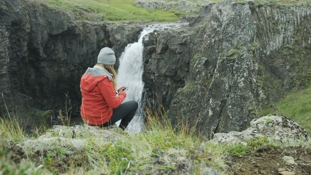 woman taking photo of waterfall with her cell phone