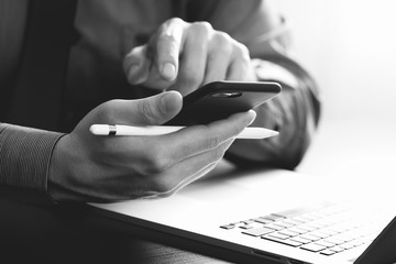 close up of businessman working with mobile phone and stylus pen and laptop computer on wooden desk...