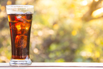 Glass of soda water with ice on the wooden table and blurred nature background
