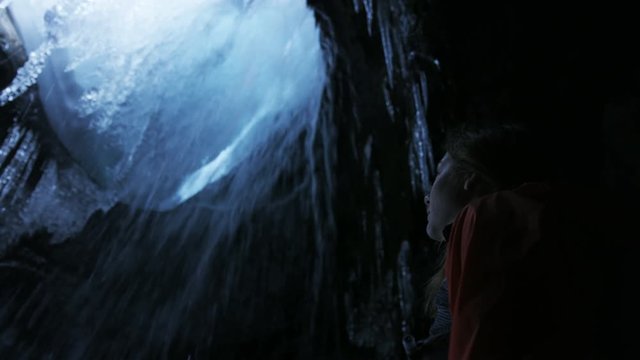 slow motion girl admiring waterfall in frozen cave