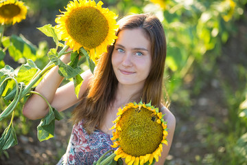 Cute beautiful young girl lady woman sitting on a field with big sunflowers.Brunette with blue eyes...