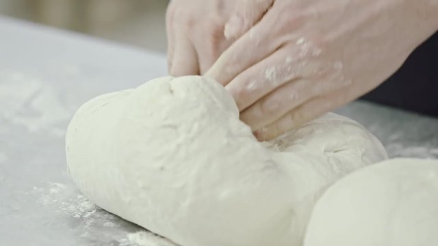 Closeup of male hands kneading dough on floury table in slow motion