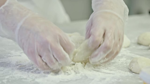 Closeup of chef hands kneading dough on floury table and using rolling pin to shape small disks