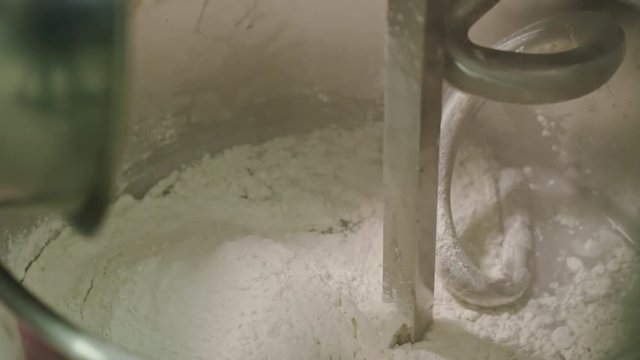 Closeup of sifting flour into dough making machine and turning it on