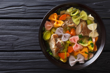 Delicious soup with meat, multi-colored farfalle pasta and vegetables close-up. Horizontal top view