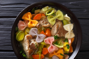 Italian soup with pork, colored farfalle pasta and vegetables close-up. horizontal top view