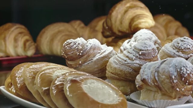 Tracking of variety of sweet pastry on shelve in bakery shop: goat cheese danishes, frosted rolls and croissants